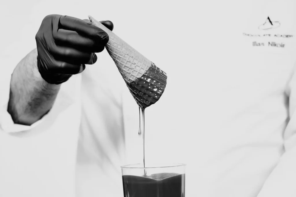 Pastry chef dipping an ice cream cone in chocolate ganache