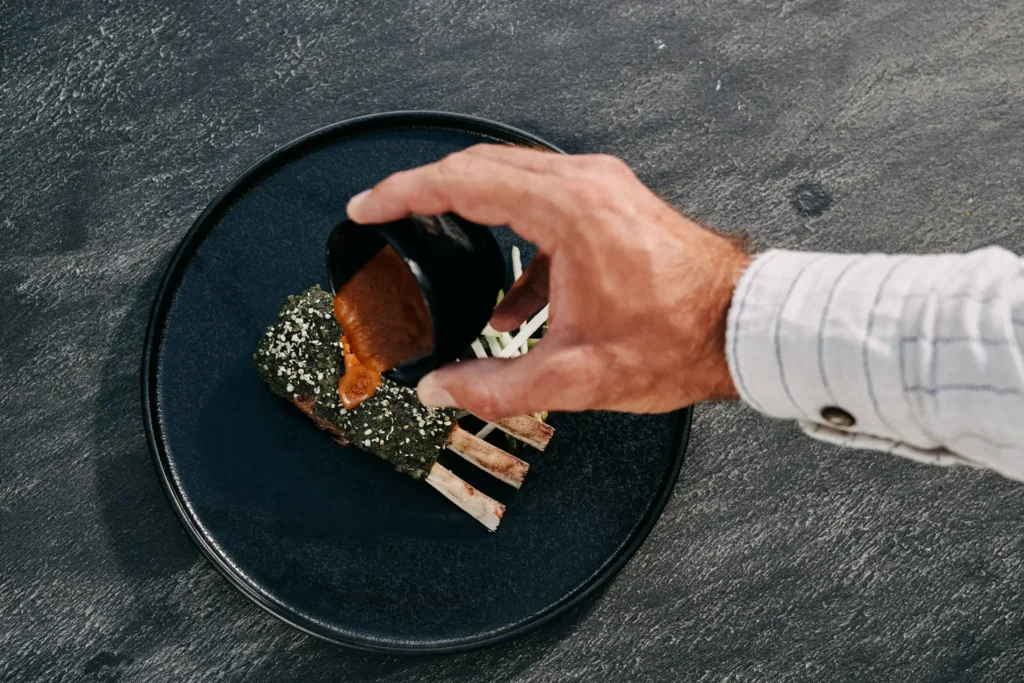 Chef finishing fine-dining plate with sauce at Lure Restaurant