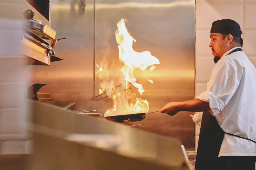 Cook preparing a dish with pan and flames in the Cupitol kitchen
