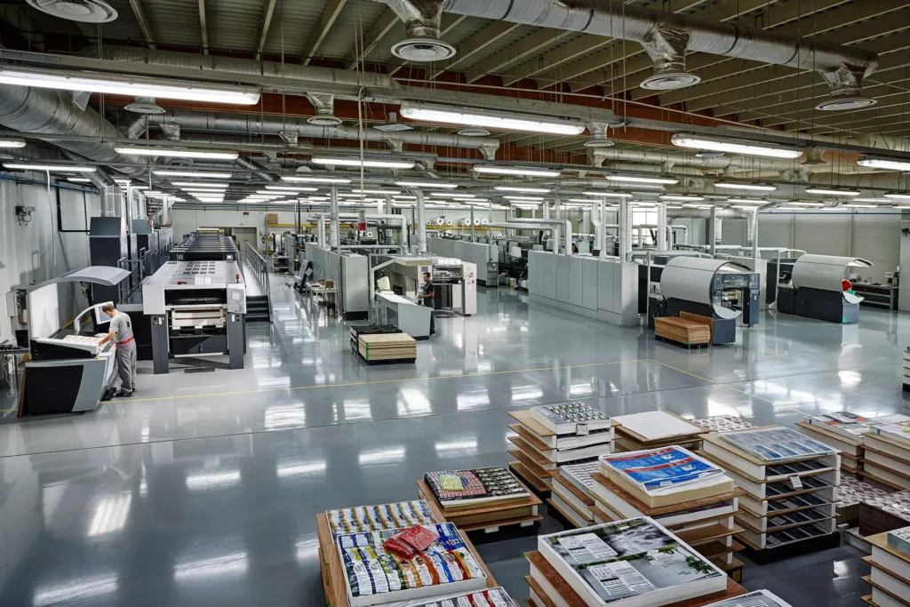Wide view of Karydakis printing machinery with stacks of colourful printed sheets in the foreground