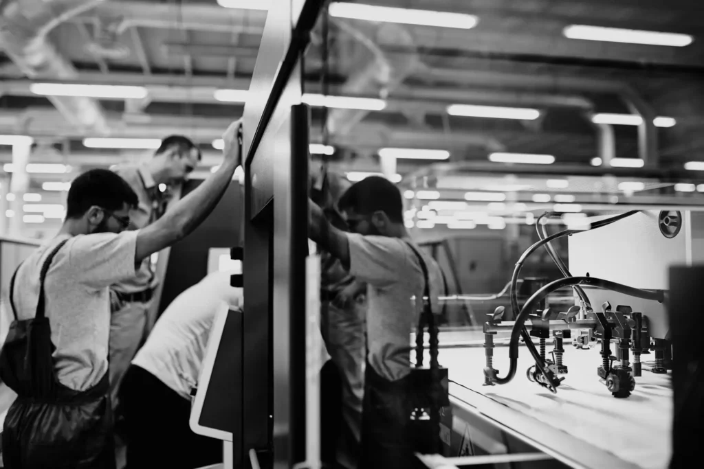 Black-and-white printing machine detail with operators reflected in its glass enclosure