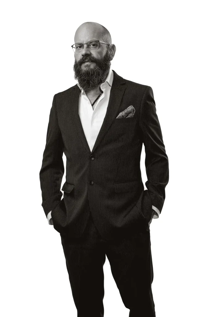 Standing studio portrait of Yannis Manikis wearing a business suit