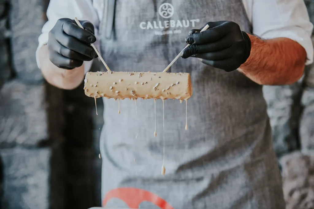 Pastry being dipped into chocolate glaze by Michalis Chatzikalimeris