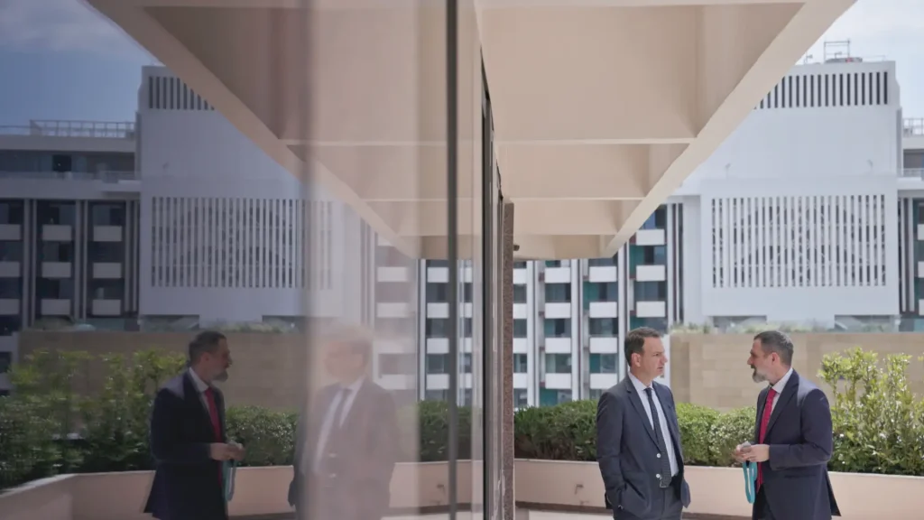Two suited men talking on an office terrace, reflected in glass, in the Dryllerakis Law Firm brand film